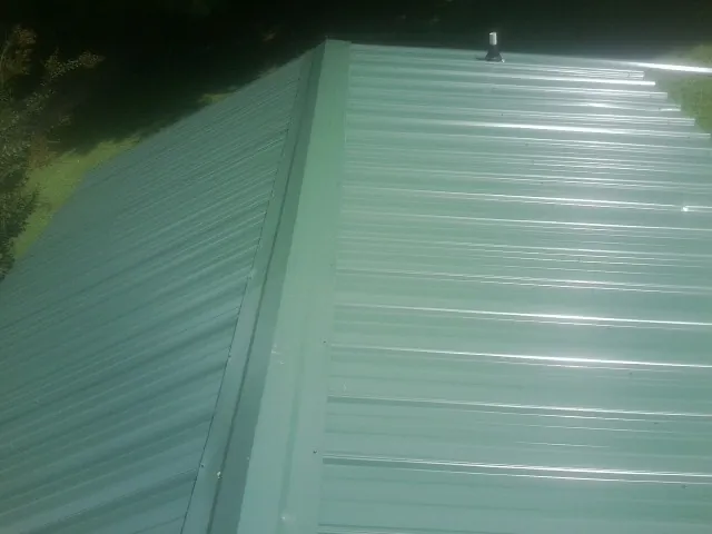 New green metal panels meeting at the ridge of a roof — Flat Roof Repair work by our crew in Mountain Home